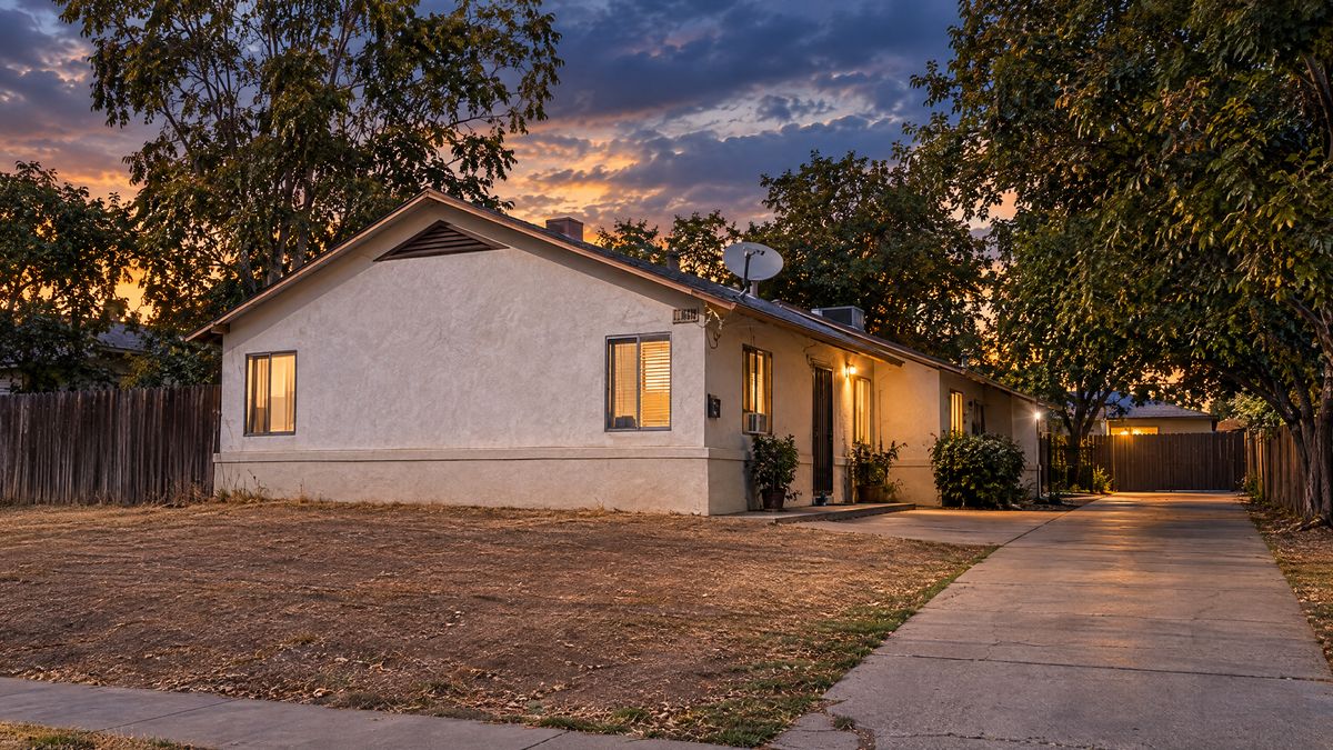 Single-story stucco home with a long driveway at dusk